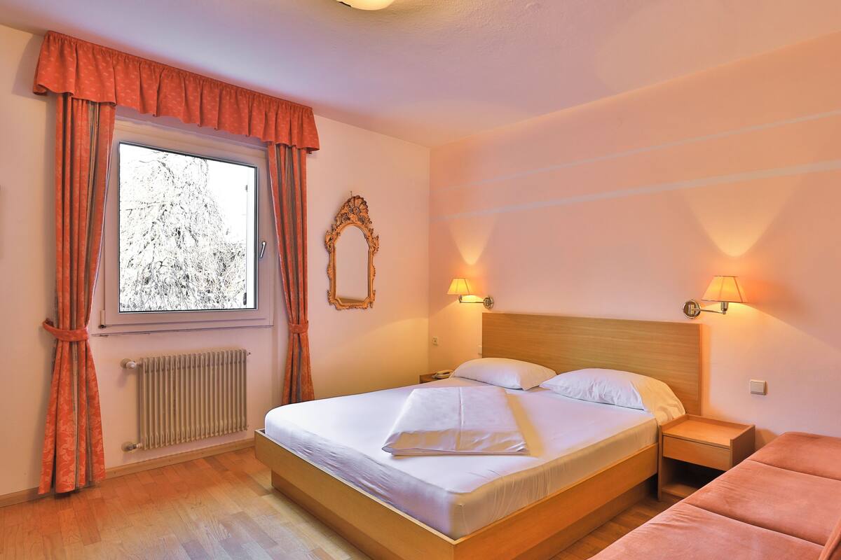 A hotel room with a bed, a nightstand, a lamp, a mirror, and a window with curtains.