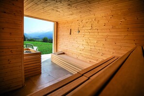 Una sauna de madera con un banco y una mesita, una ventana con vistas a las montañas, y un revestimiento de madera.