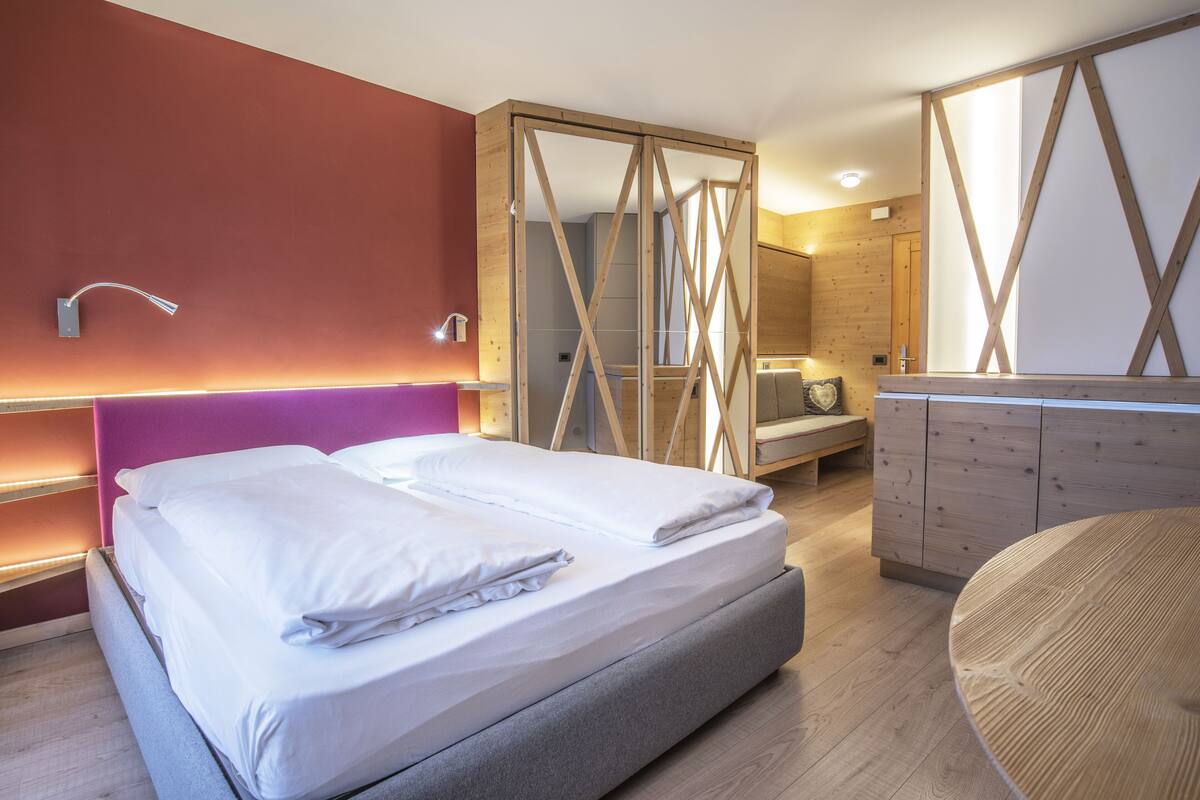 A modern bedroom with a large bed, a wooden wardrobe, and a built-in bench.