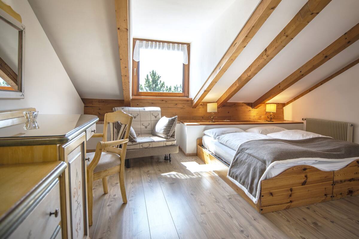 A cozy attic bedroom with a loft bed, a small desk, and a chair.