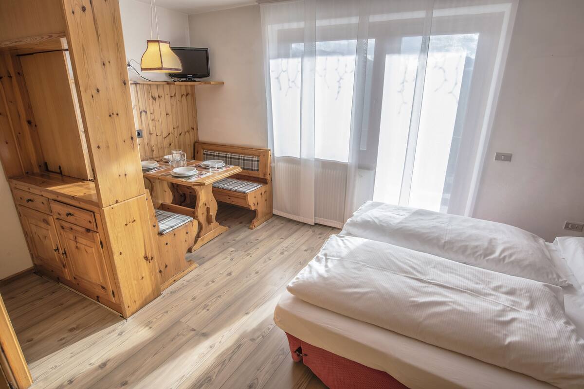 A bedroom with a bed, a wooden desk, a chair, and a television on a shelf.