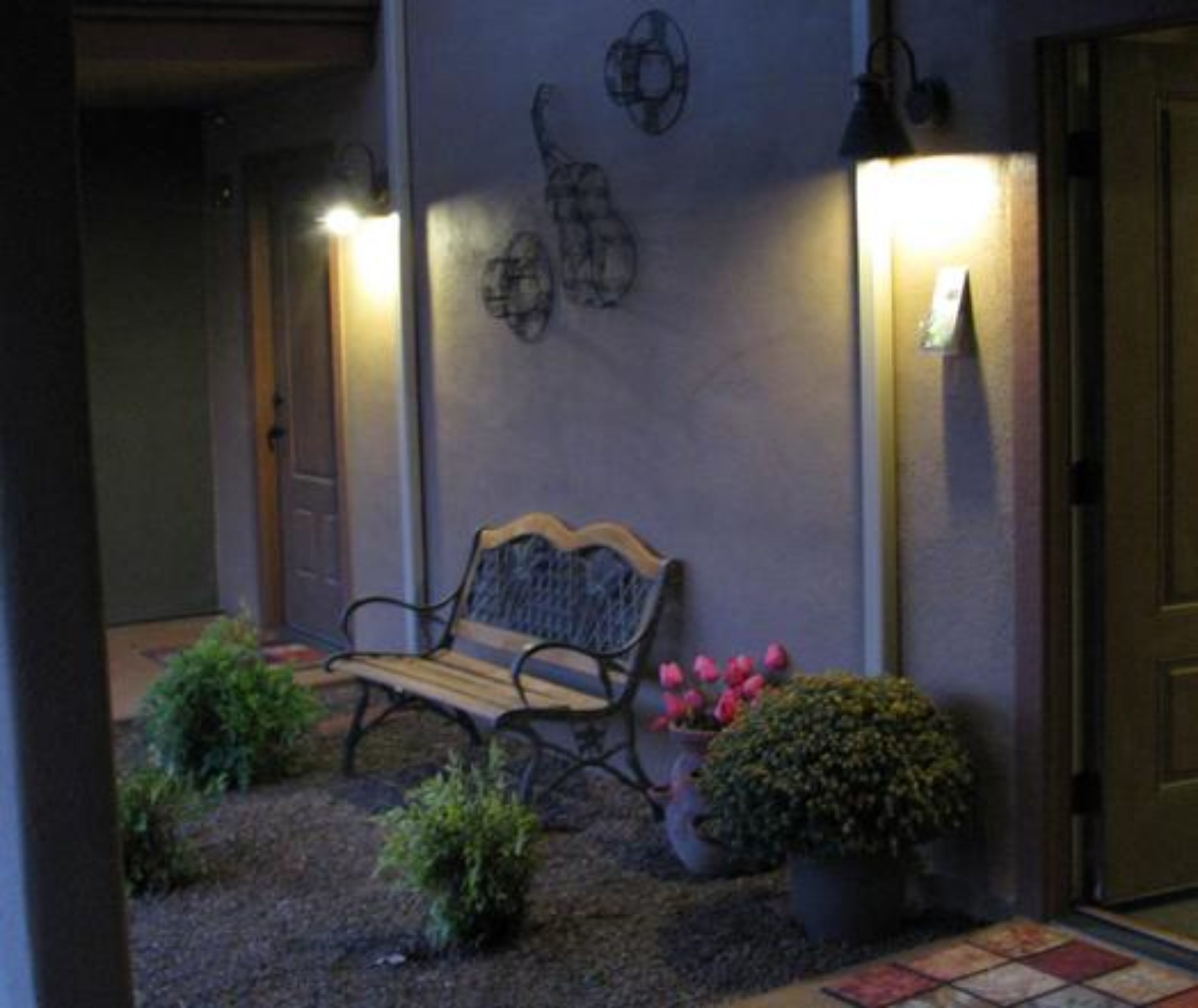 A bench outside a building with a door, a wall-mounted light fixture, and potted plants.