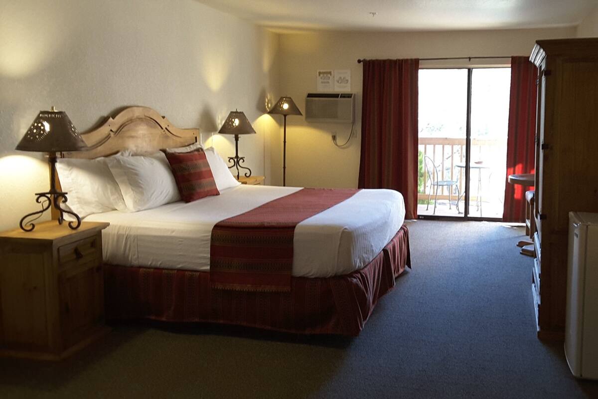 Une chambre d’hôtel équipée d’un lit, de lampes de chevet, d’un bureau, d’un réfrigérateur et d’une porte-fenêtre coulissante donnant sur le balcon.