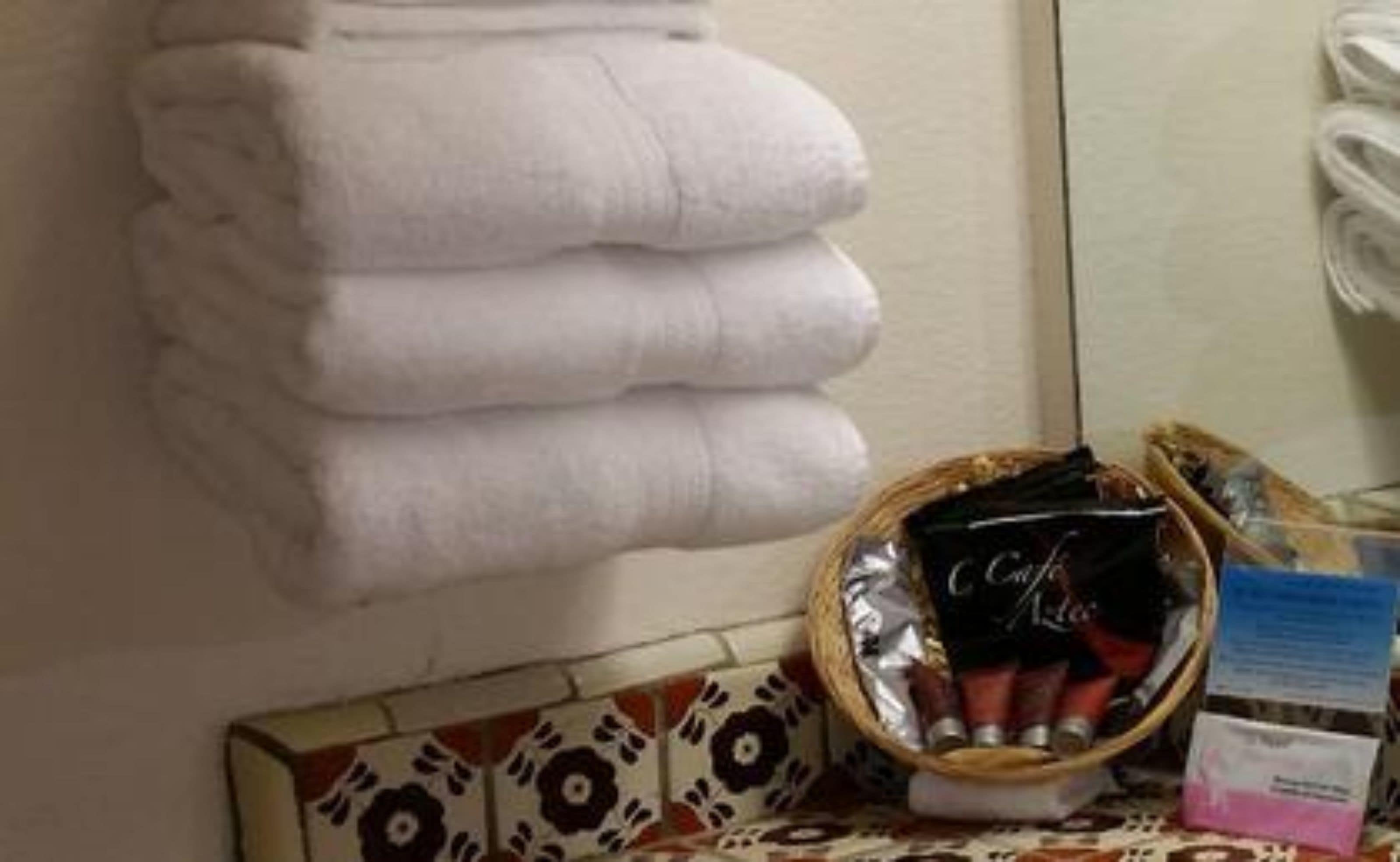 Une pile de serviettes blanches, un panier rempli de produits de toilette et un mur recouvert de carreaux décoratifs.