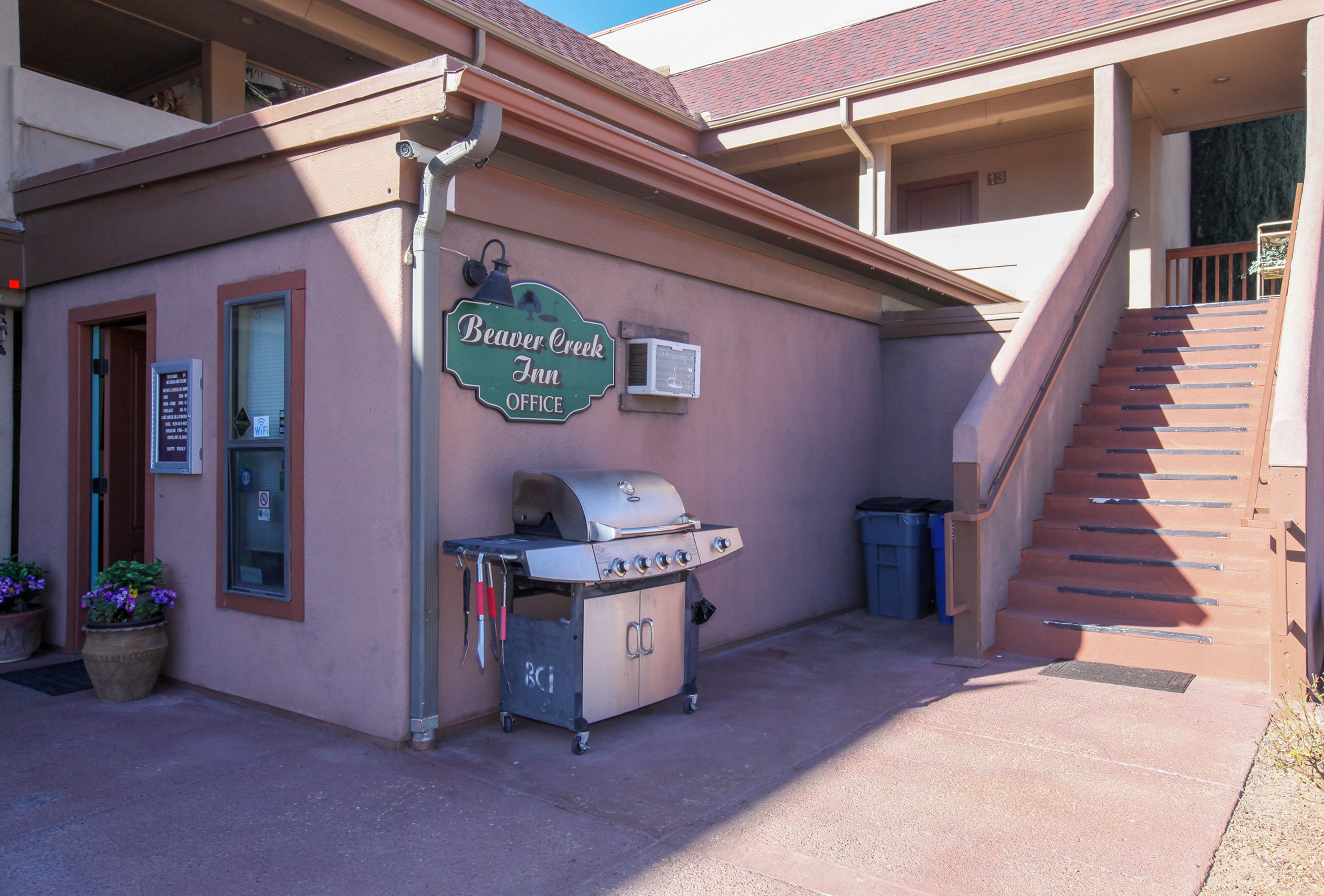 A building with a sign reading "Beaver Creek Inn Office," a barbecue grill, and a staircase leading to an upper level.
