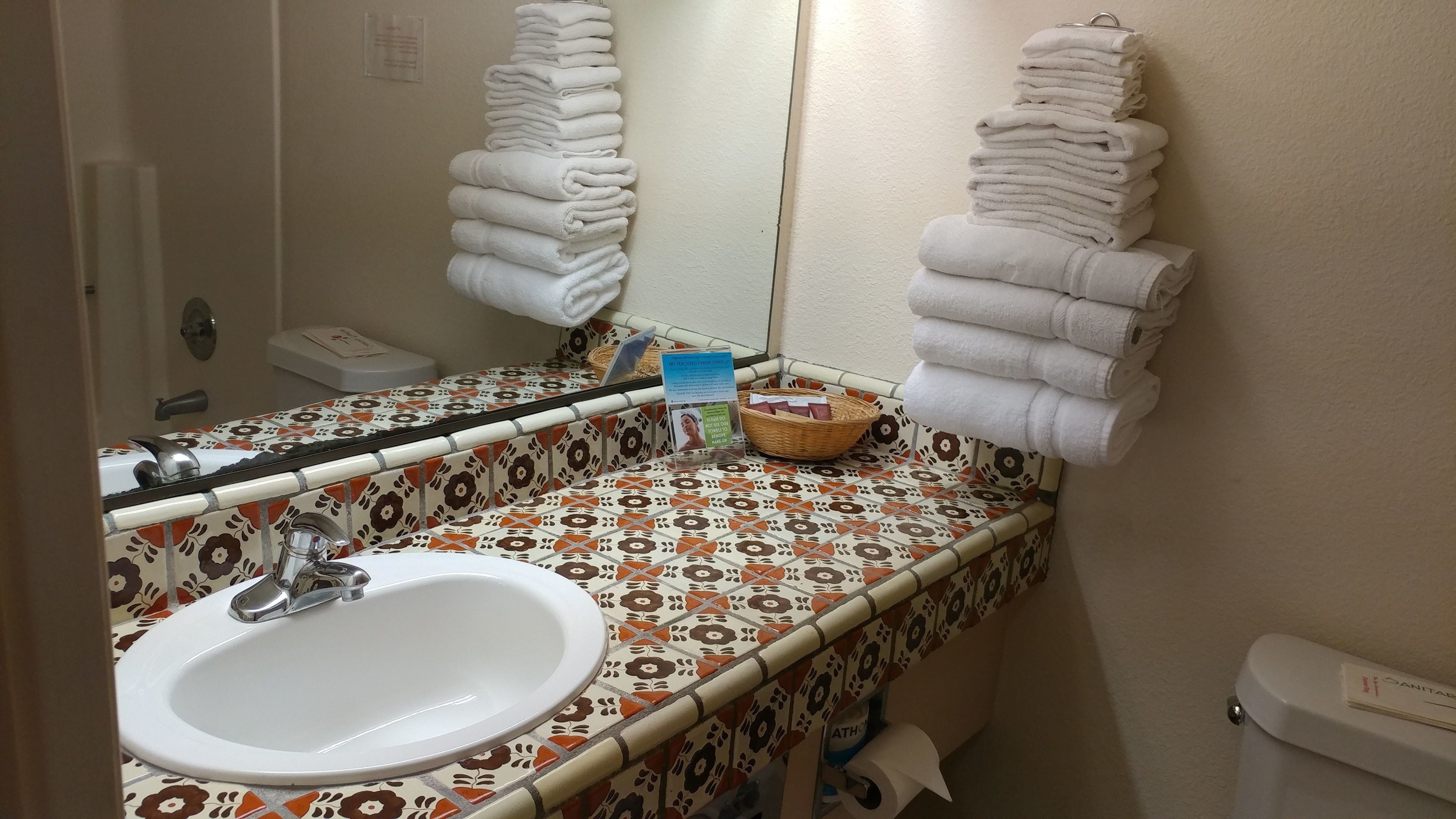 A bathroom with a white sink, a mirror, and two stacks of white towels.