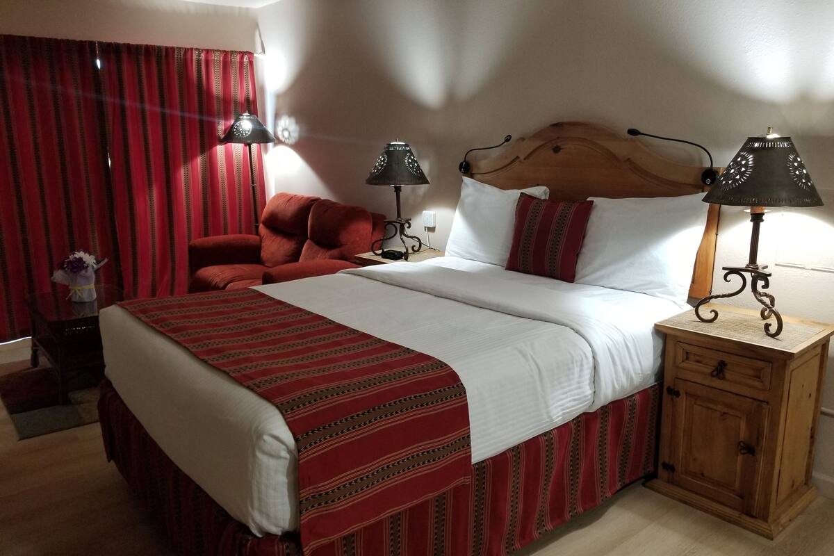 Une chambre d’hôtel avec un grand lit, deux lampes de chevet, une table de chevet en bois et une chaise rouge.