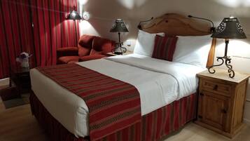 A hotel room with a large bed, two bedside lamps, a wooden nightstand, and a red chair.