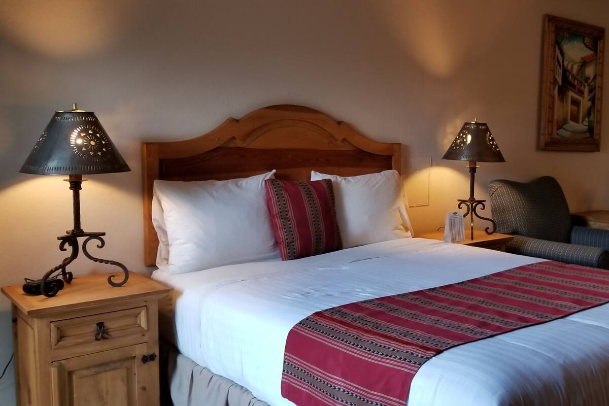 Un lit bien fait, recouvert d’une couverture à rayures rouges et blanches, deux tables de chevet avec des lampes, une tête de lit en bois, une chaise et un tableau accroché au mur.