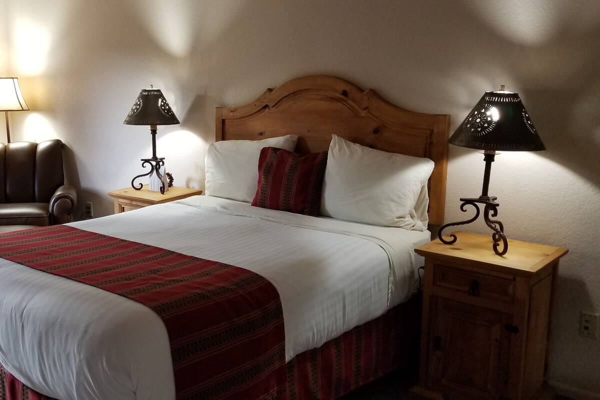 Un lit bien fait, recouvert d’une couvre-lit rouge et blanche, deux lampes de chevet, une table de chevet en bois, un fauteuil en cuir et un climatiseur fixé au mur.