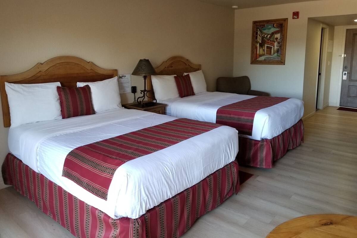 Une chambre d’hôtel avec deux lits, chacun recouvert de draps blancs et d’une couvre-lit à rayures rouges. On y trouve une tête de lit en bois, une table de chevet avec une lampe et un tableau accroché au mur.