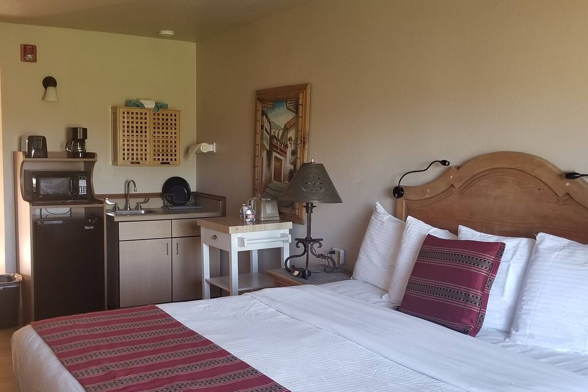 Une chambre d’hôtel équipée d’un lit, d’un bureau avec une lampe, d’un four à micro-ondes, d’une machine à café et d’un petit réfrigérateur.
