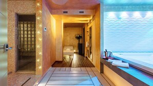 A modern spa room with a wooden floor, a massage table, a bathtub, and a decorative wall with a wavy pattern.