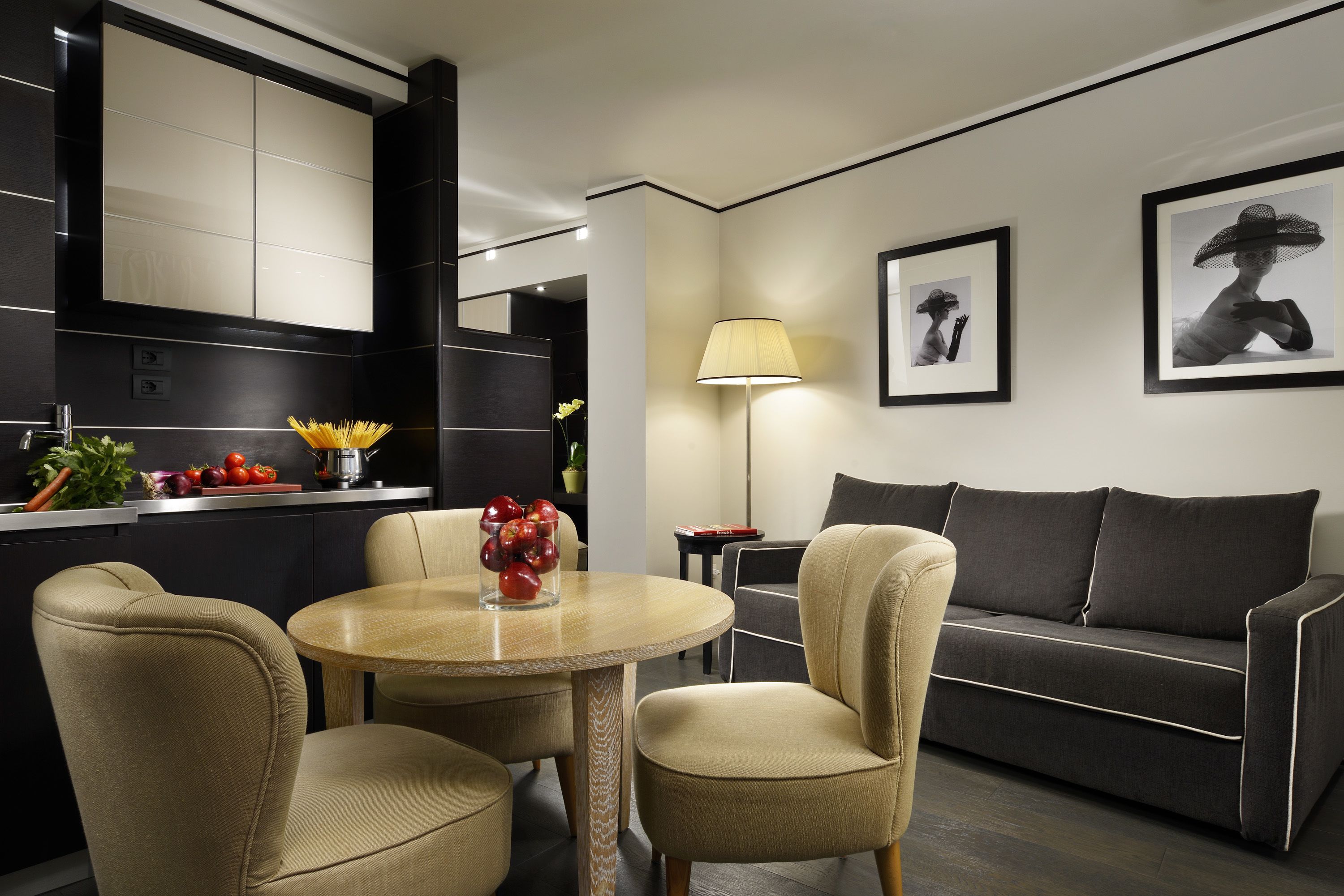 A modern living room with a sofa, a round table, and two chairs. There is a kitchen area with a counter and cabinets.