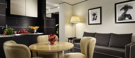 A modern living room with a sofa, a round table, and two chairs. There is a kitchen area with a counter and cabinets.