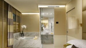 A modern hotel room with a bed, a glass-enclosed shower area, a vanity with a mirror, and a small bedside table.