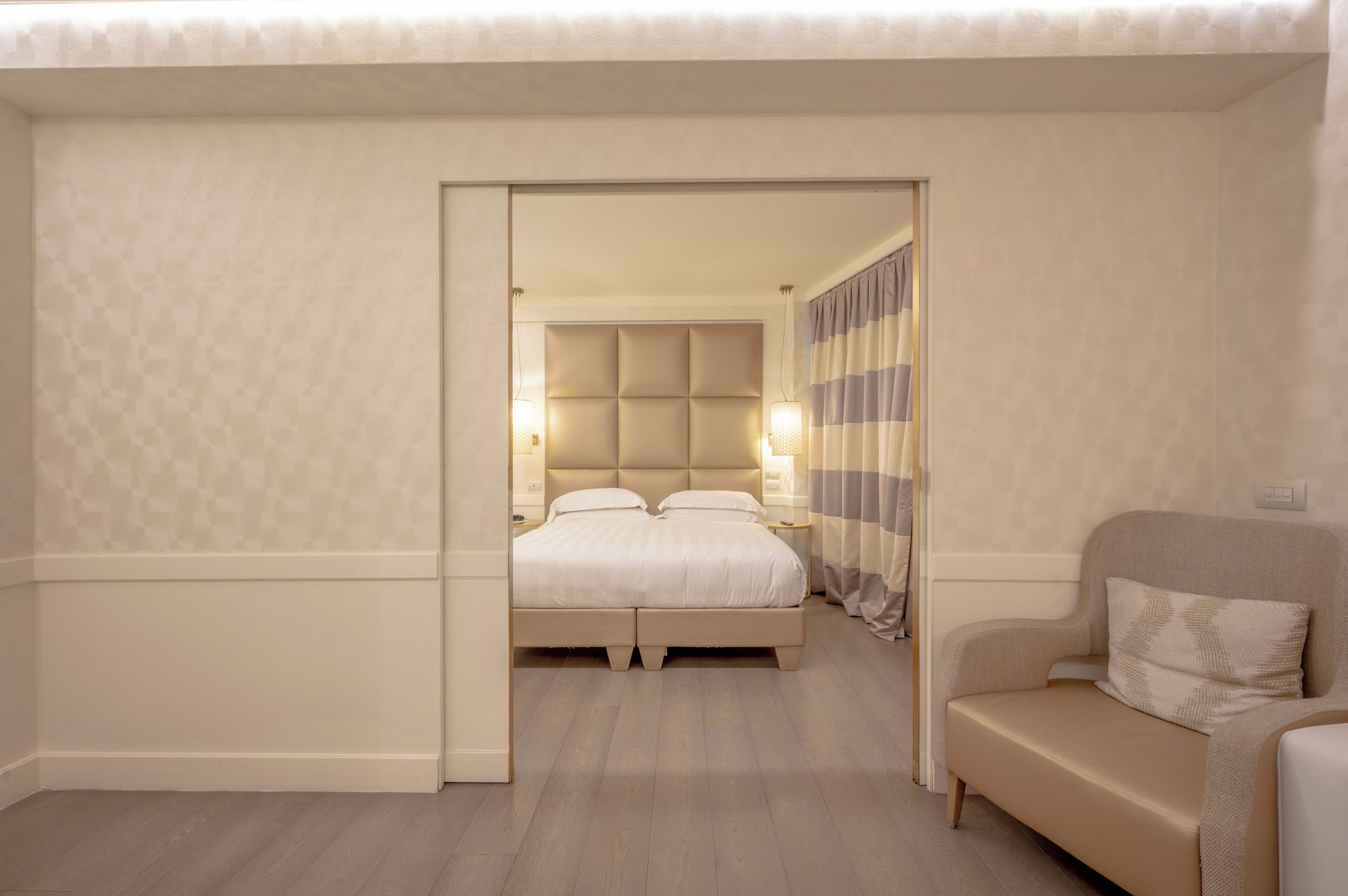A bedroom with a bed, bedside lamps, a sofa, and a curtain.