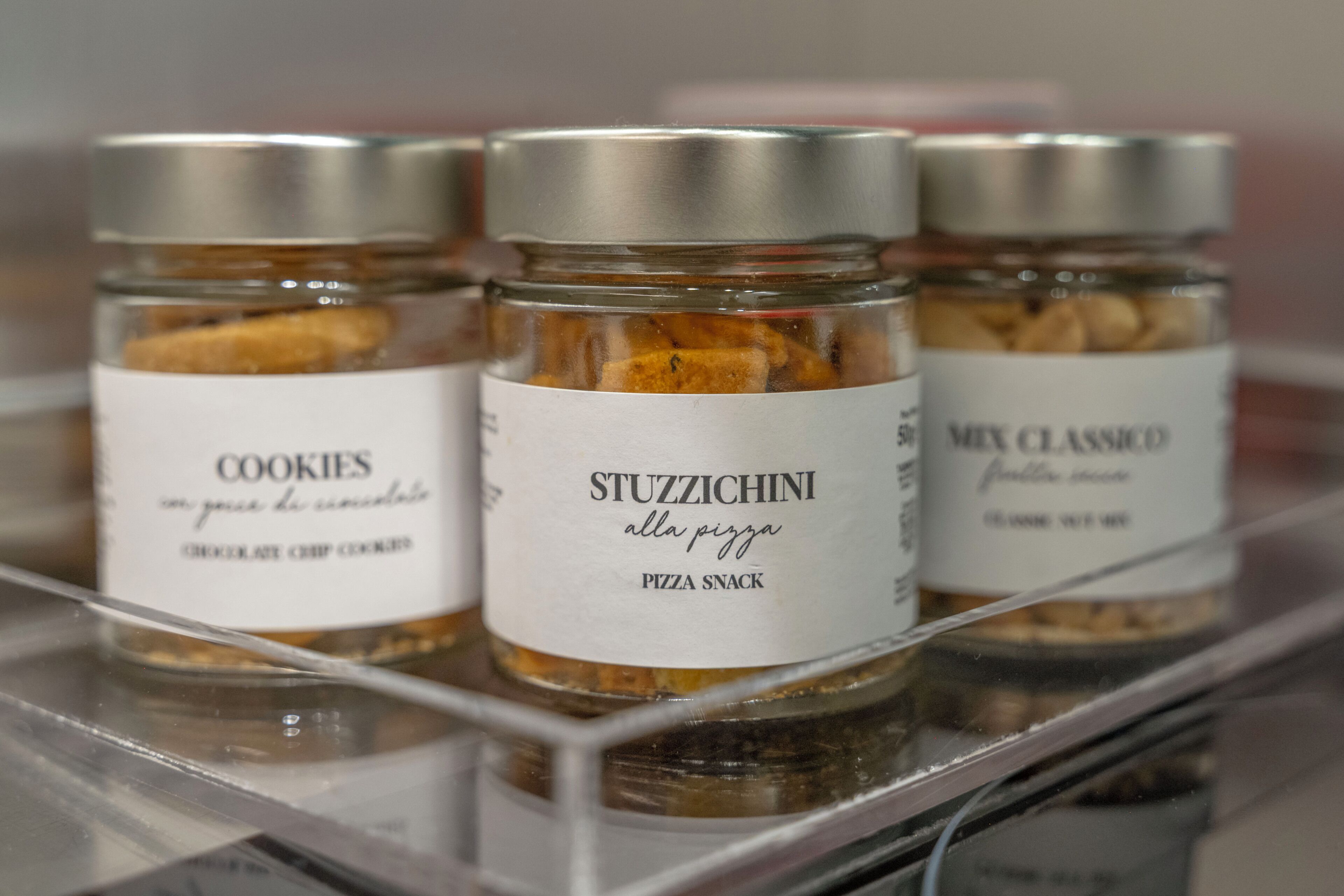 Trois pots de biscuits et un pot de snacks au goût pizza sont posés sur une étagère.