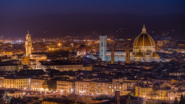 A nighttime cityscape with prominent historical buildings, including a tower and a dome.