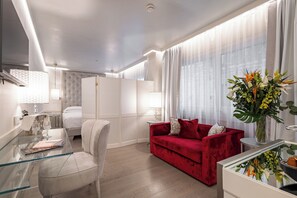 A modern hotel room with a glass dining table, a red sofa, a white bed, and a large window with sheer curtains. - Ponte Vecchio Suites & Spa (Florence)