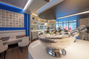A modern bar area with a large ice bucket filled with bottles, a seating area with white cushioned benches, and a decorative wall with circular patterns. - Ponte Vecchio Suites & Spa (Florence)