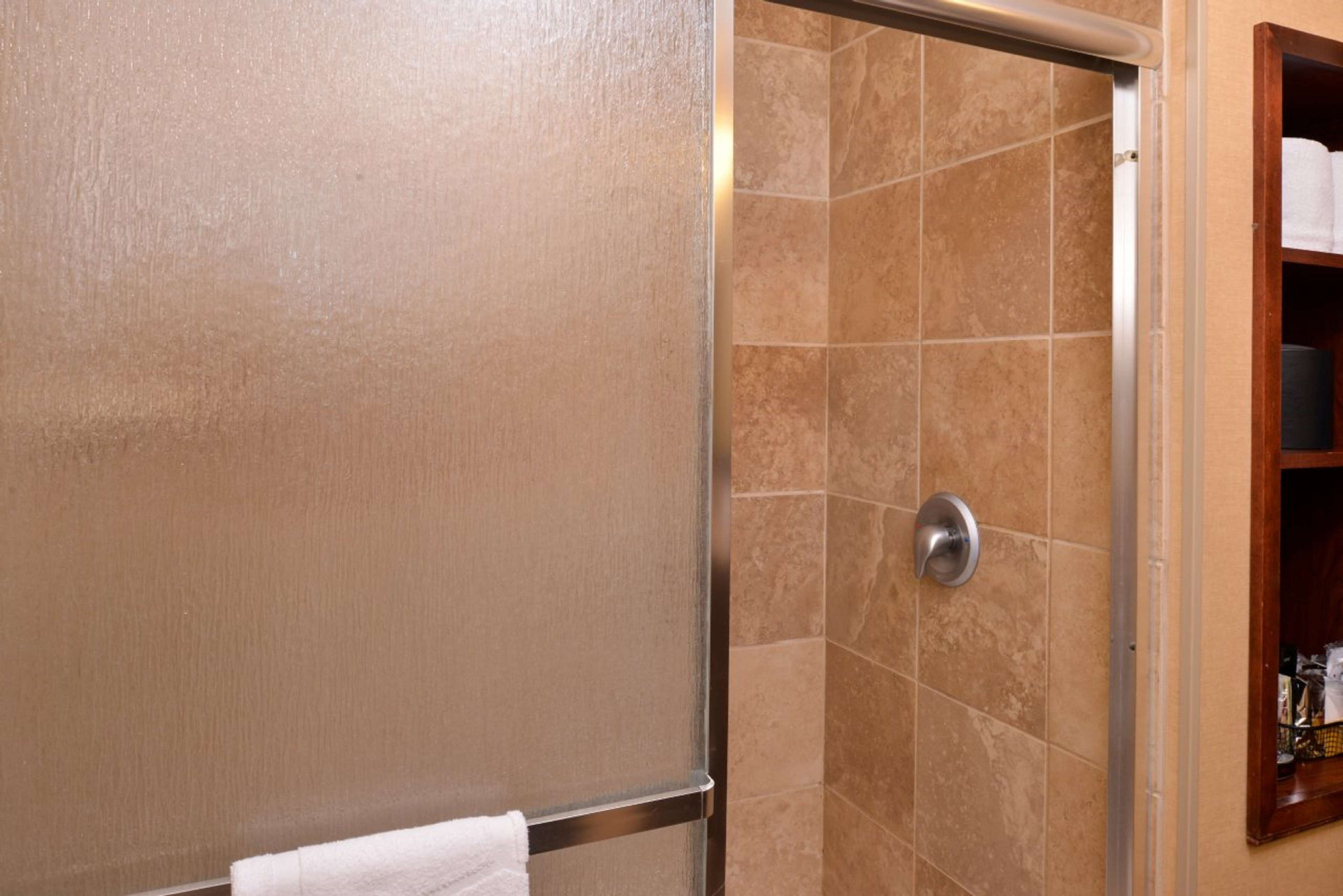 A bathroom with beige walls, a shower with beige tiles, and a towel rack with a white towel.
