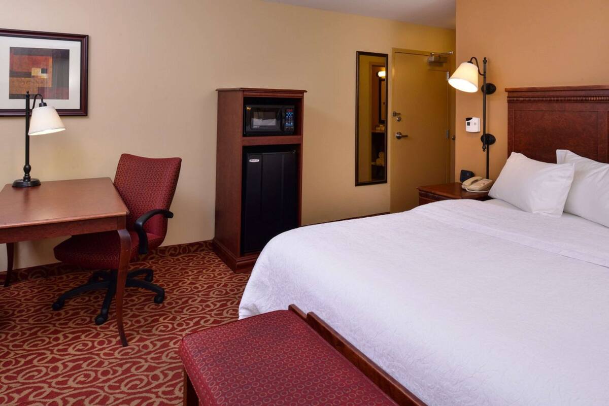 Hotelkamer met een bed, bureau, stoel, magnetron, telefoon en spiegel.