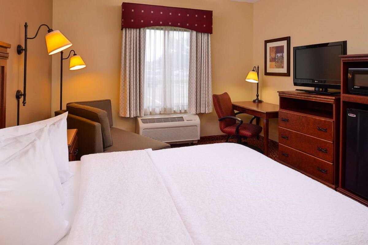 Een hotelkamer met een bed, een bureau, een stoel, een televisie en een dressoir.