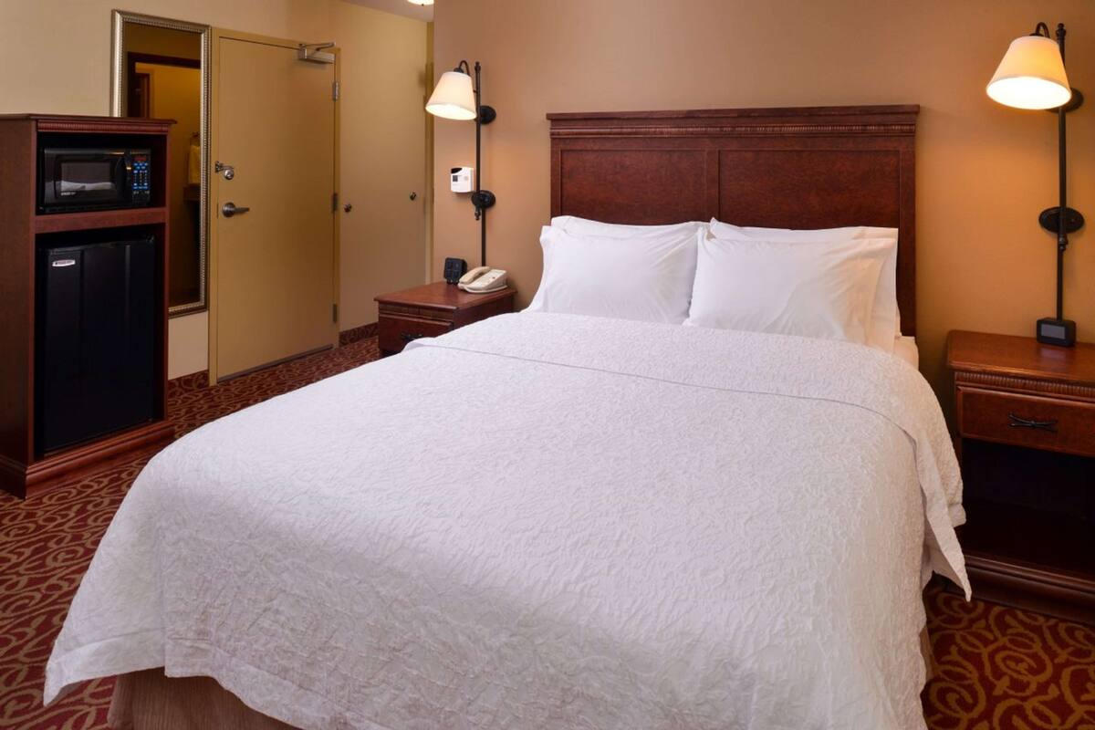 Een hotelkamer met een groot bed, een houten hoofdeinde, een nachtkastje met een lamp, een telefoon en een minibar.