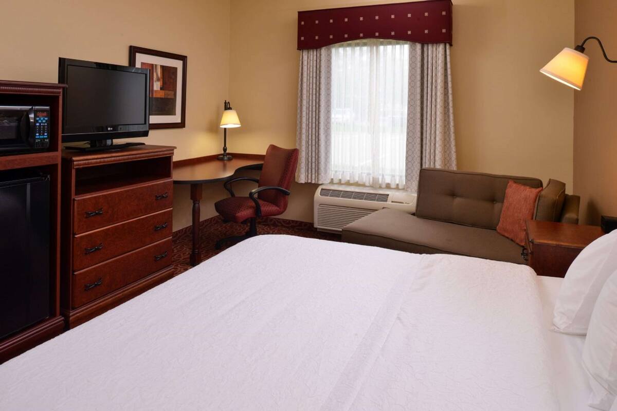 Een hotelkamer met een bed, een bureau met een computer, een stoel, een magnetron en een televisie.