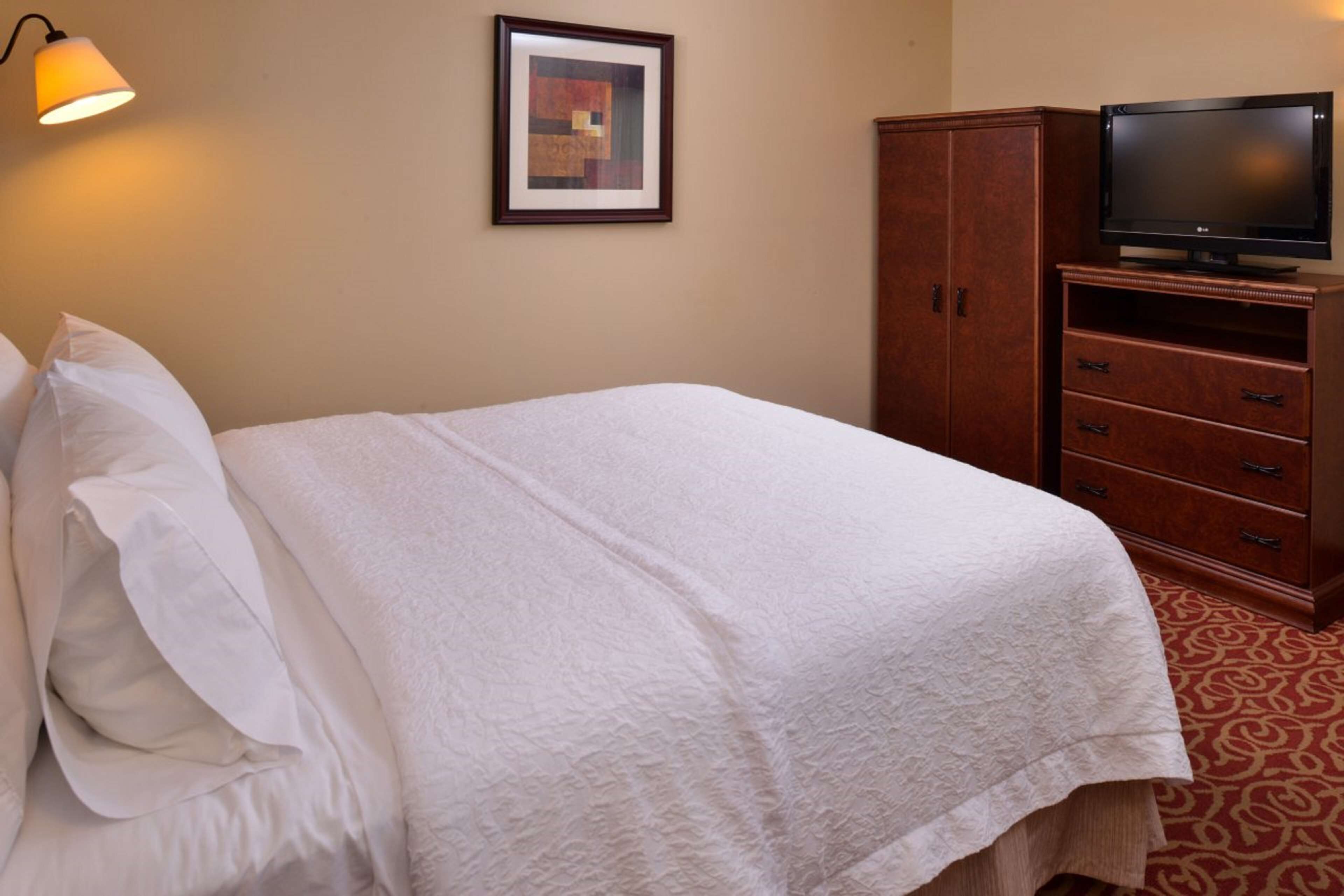 Une chambre d’hôtel avec un lit soigneusement fait, un téléviseur posé sur une commode en bois et un tableau encadré accroché au mur.