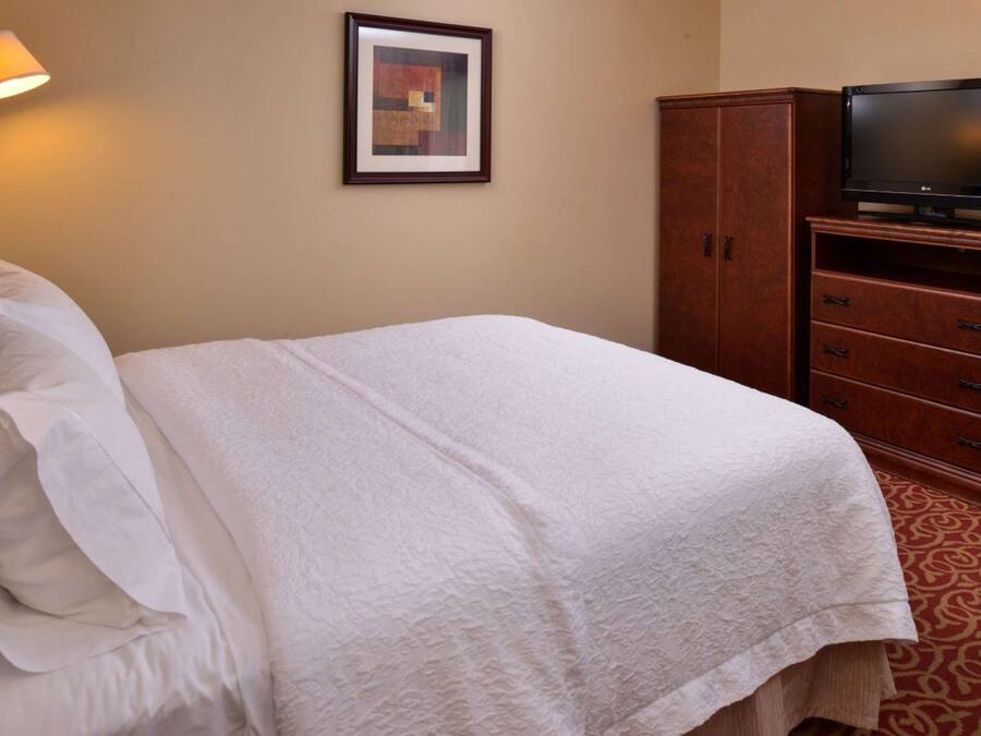 Une chambre d’hôtel avec un lit soigneusement fait, un téléviseur posé sur une commode en bois et un tableau encadré accroché au mur.