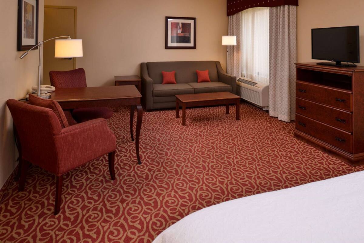 Een hotelkamer met een bank, fauteuil, bureau en kapstok.