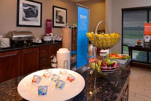 A hotel breakfast area with a buffet setup including a fruit bowl, a coffee station, and a beverage dispenser. - Hampton Inn by Hilton Lincoln (Lincoln)