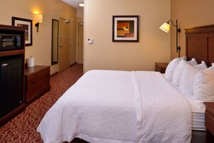 Una habitación de hotel con una cama grande, un microondas, un aparador y un cuadro en la pared.