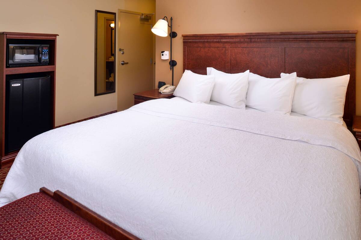 Een hotelkamer met een groot bed, een nachtkastje met een lamp, een telefoon en een minibar.