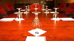 Una mesa de conferencias con un jarrón de vidrio en el centro, rodeada de sillas y servilletas blancas con un logotipo.