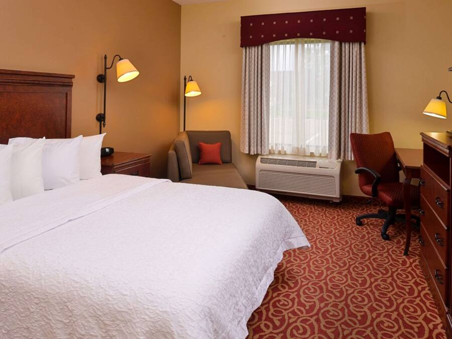 A hotel room with a large bed, two bedside tables, a desk, a chair, and a window with curtains.