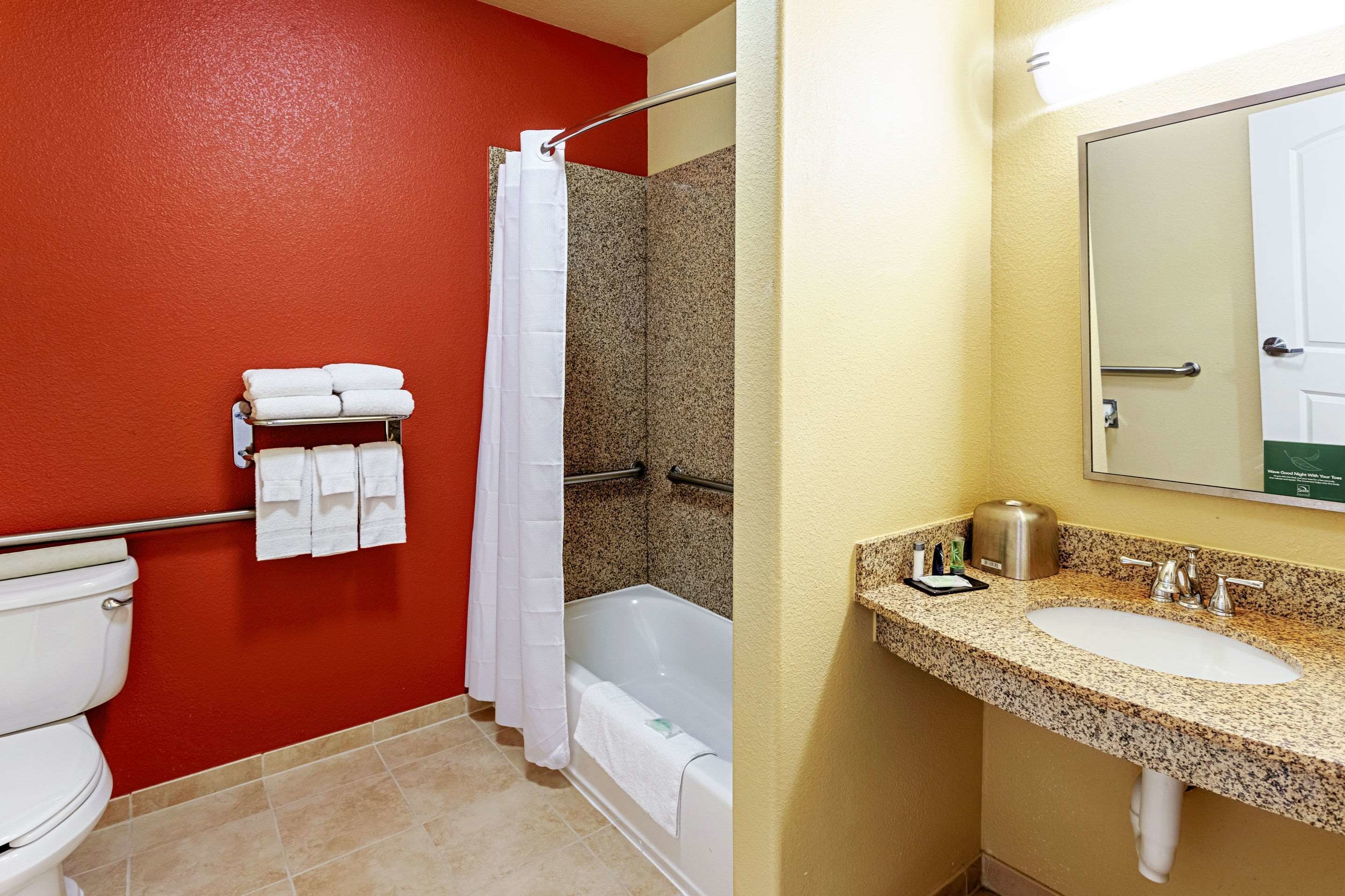 Ein Badezimmer mit roter Wand, einer weißen Badewanne, einer weißen Toilette und einem Waschbecken mit einer Granit-Arbeitsplatte.