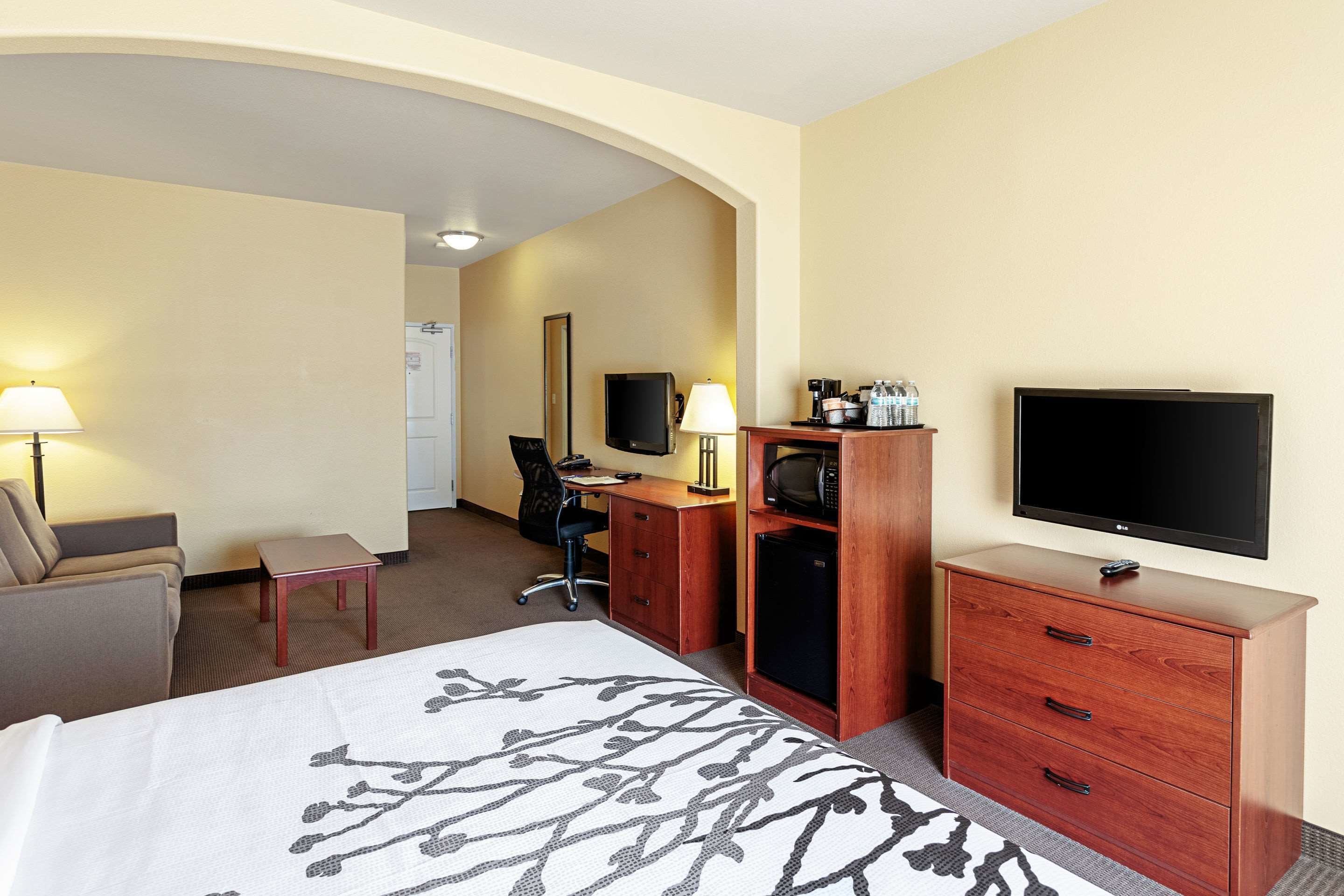 A hotel room with a bed, desk, chair, television, and a minibar.