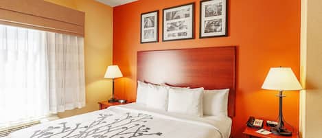 A hotel room with a large bed, two bedside tables with lamps, a wooden headboard, and three framed pictures on the wall.