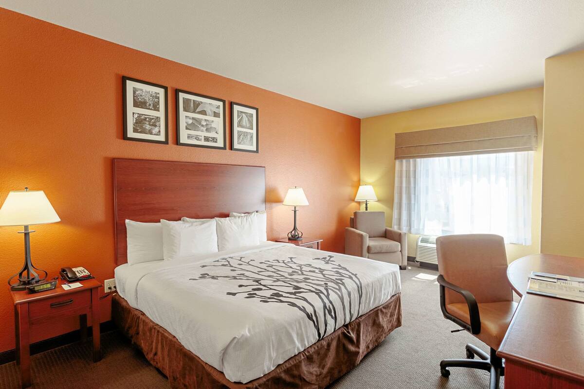 A hotel room with a large bed, two bedside tables with lamps, a desk, and a chair. There are framed pictures on the wall above the bed.