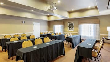 Uma sala de conferências com várias mesas e cadeiras, um projetor e quadros nas paredes.
