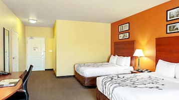 Habitación de hotel con dos camas, un escritorio y una silla. Se ve una puerta y una pared con cuadros.