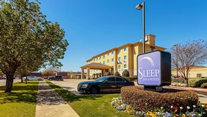Een Sleep Inn & Suites met een helder zicht op de ingang, een parkeerplaats en een goed onderhouden tuin met kleurrijke bloemen.