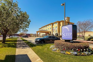 Un Sleep Inn & Suites con vistas despejadas a la entrada, un estacionamiento y un jardín bien cuidado con flores coloridas.