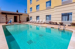 Una piscina con sillones de descanso y un edificio con grandes ventanales.