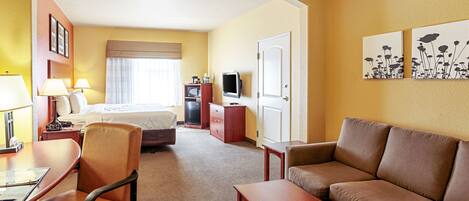 A hotel room with a bed, a desk with a chair, a sofa, a television, and artwork on the walls.
