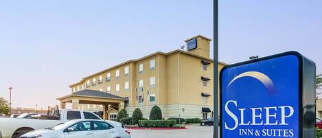 A hotel sign with the name "Sleep Inn & Suites" and a building with multiple windows and balconies in the background.