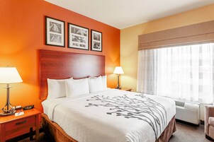 Una habitación de hotel con una cama grande, dos mesitas de noche con lámparas, un cabecero y una ventana con cortinas.